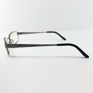 May include: Silver-toned eyeglasses with a decorative floral pattern on the temples. The frames have a rectangular shape with clear lenses. The earpieces are black and curved for a comfortable fit. The glasses are set against a white background.