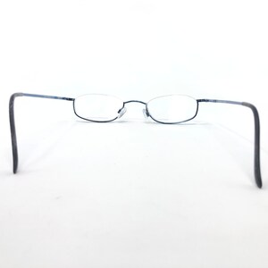 May include: A pair of rimless eyeglasses with a dark blue metal frame. The lenses are oval-shaped and clear. The temples are dark gray and curve downward. The glasses are set against a white background.