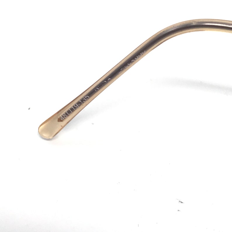 May include: Close-up of the arm of a pair of eyeglasses. The arm is a light tan color and has the numbers "48[]19-135" printed on it. The arm curves slightly and has a rounded end.