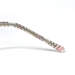 May include: Close-up of a patterned eyeglass arm. The arm features a floral design in pink, white, and tan. The text "Sassavare 100046" is printed on the arm. The end of the arm is clear.