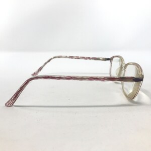 May include: A pair of eyeglasses with clear lenses and a light-colored frame. The temples feature a textured pattern with red and white stripes. The frame has a subtle, translucent appearance, and the lenses are clear.