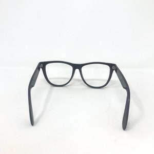 May include: Black-framed eyeglasses with a classic design. The glasses have a rectangular shape and are set against a white background. The arms of the glasses are extended, showcasing the hinges and overall structure.
