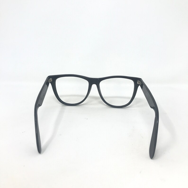 May include: Black-framed eyeglasses with a classic design. The glasses have a rectangular shape and are set against a white background. The arms of the glasses are extended, showcasing the hinges and overall structure.