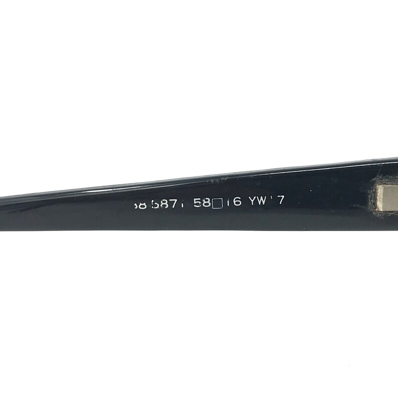 May include: Black eyeglass frame arm with the numbers and letters: 58587, 58 16 YW'7. The frame is glossy and rectangular. The arm is angled slightly upward.