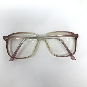 May include: Clear eyeglasses with a light brown and purple frame. The glasses have a rectangular shape and are viewed from above. The lenses are clear, and the arms are a light purple color.