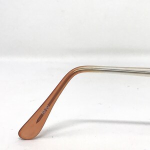 May include: Close-up of eyeglasses arm with a light brown, curved temple and a silver-colored arm. The text "52-20" is printed on the temple. The glasses are set against a white background.
