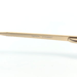 May include: Close-up of a gold-colored metal object with the text "GERDA 21046957" etched on its surface. The object has a sleek, modern design and appears to be a part of a larger item, possibly eyewear or jewelry.