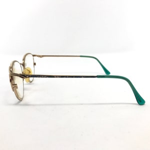 Pu&ograve; includere: Occhiali in metallo dorato con aste in plastica verde. Gli occhiali hanno una montatura rettangolare e lenti trasparenti.