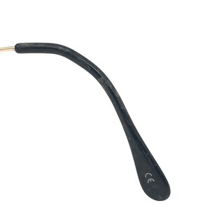 May include: Close-up of a black eyeglass arm with a gold-coloured hinge. The arm is curved and has a matte finish. The letters "CE" are printed on the inside of the arm.