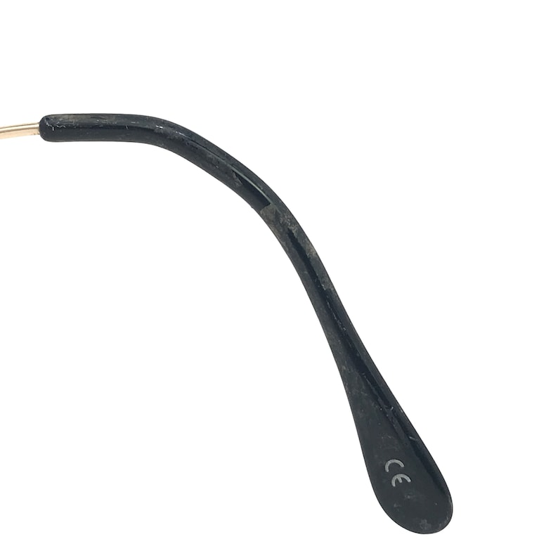 May include: Close-up of a black eyeglass arm with a gold-coloured hinge. The arm is curved and has a matte finish. The letters "CE" are printed on the inside of the arm.