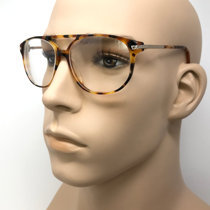K&ouml;nnte beinhalten: Schildpatt-Brille mit klaren Gl&auml;sern. Die Brille hat einen Metallrahmen und einen silbernen Akzent an der Seite.