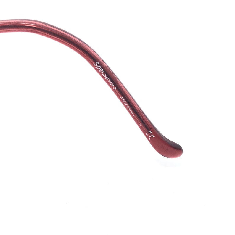 Puede incluir: Primer plano de una parte de unas gafas. La montura es de color marr&oacute;n rojizo oscuro. El texto "Specsavers" est&aacute; impreso en blanco a lo largo de la varilla. La varilla se curva hacia abajo, terminando en una punta redondeada.