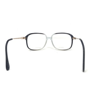 May include: Square-framed spectacles with a gradient black to clear frame. The temples are silver-toned metal, and the earpieces are black. The glasses are set against a white background.