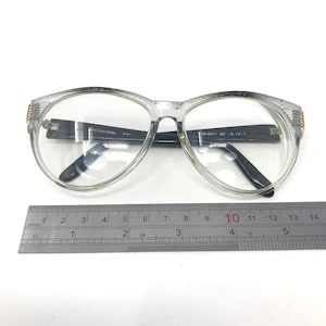 May include: Clear plastic eyeglasses with black arms and gold accents. The arms are labeled "SPECSAVERS 73C" and "08-5871 58 16 YW17". The eyeglasses are measured on a ruler, showing they are approximately 10 centimeters wide.