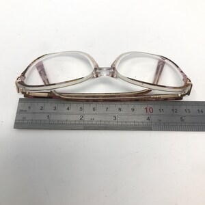 May include: Clear-framed eyeglasses with a rectangular shape, featuring a decorative pattern on the temples. The glasses are approximately 5.5 inches wide, measured with a ruler. The lenses are clear, and the frame is a mix of clear and patterned materials.