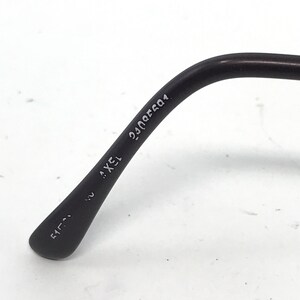 May include: Close-up of a black eyeglass arm with the text "AXEL 15" and other numbers. The arm curves slightly and has a matte finish. The background is white.