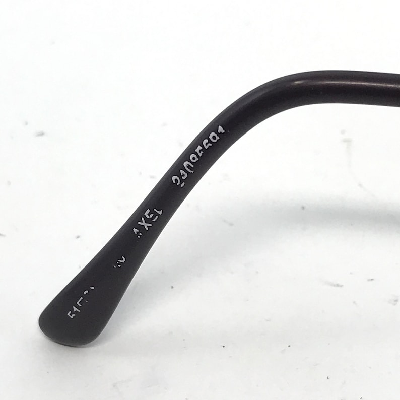 May include: Close-up of a black eyeglass arm with the text "AXEL 15" and other numbers. The arm curves slightly and has a matte finish. The background is white.