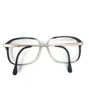 May include: Eyeglasses with a black and clear frame and black temples. The glasses have a rectangular shape with a silver-coloured metal bridge and accents. The lenses are clear.