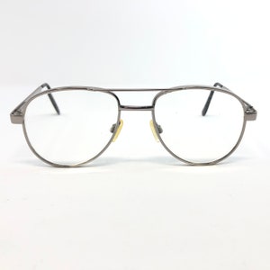 Peut inclure: Une paire de lunettes de style aviateur avec une monture en m&eacute;tal canon de fusil. Les verres sont clairs et les plaquettes nasales sont jaunes. Les lunettes ont un double pont et des branches fines. Le design est &eacute;pur&eacute; et moderne.