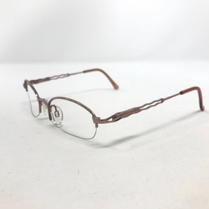 May include: A pair of eyeglasses with a half-rim design. The frames are a muted brown color with a wavy design on the temples. The lenses are clear, and the arms are a darker brown.
