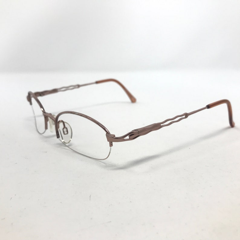 May include: A pair of eyeglasses with a half-rim design. The frames are a muted brown color with a wavy design on the temples. The lenses are clear, and the arms are a darker brown.