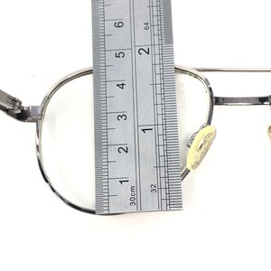 Peut inclure: Des lunettes &agrave; monture argent&eacute;e avec des verres transparents sont mesur&eacute;es avec une r&egrave;gle. Les lunettes ont une forme classique et ronde et des plaquettes nasales. La r&egrave;gle indique les mesures en centim&egrave;tres.