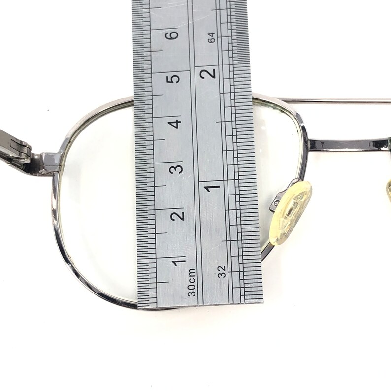 Peut inclure: Des lunettes &agrave; monture argent&eacute;e avec des verres transparents sont mesur&eacute;es avec une r&egrave;gle. Les lunettes ont une forme classique et ronde et des plaquettes nasales. La r&egrave;gle indique les mesures en centim&egrave;tres.