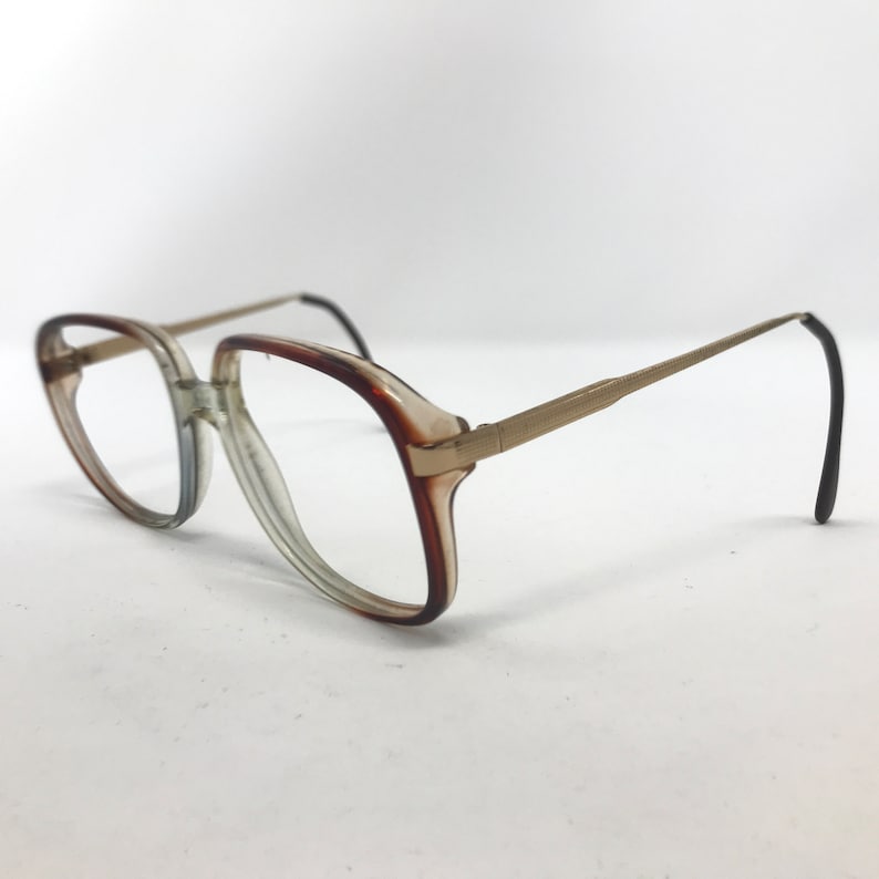 Op de afbeelding: Een vintage bril met een helder en bruin plastic montuur en goudkleurige metalen pootjes. De lenzen zijn helder en de oorpuntjes zijn zwart. De bril staat tegen een witte achtergrond.