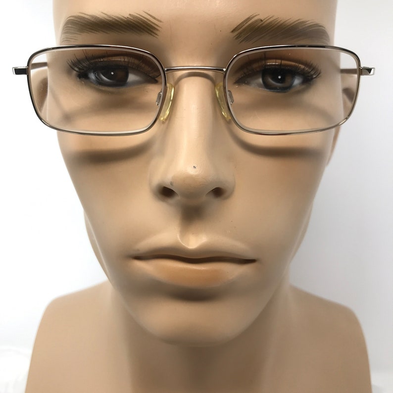 May include: Silver-framed eyeglasses with rectangular lenses. The glasses have a thin, metallic frame and are displayed on a mannequin head. The lenses are clear, and the overall design is simple and classic. The glasses are suitable for everyday use.