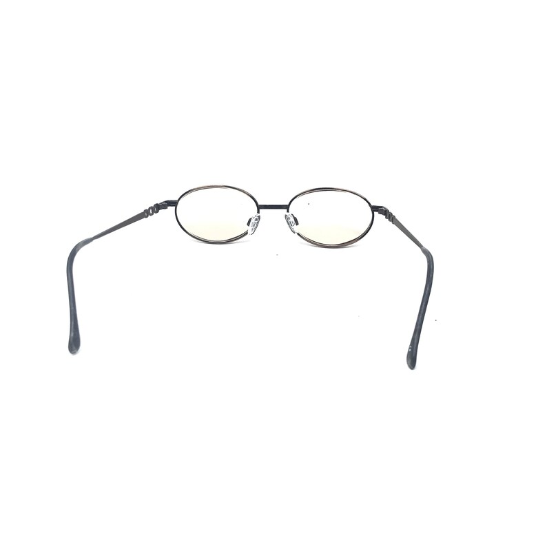 May include: Oval-shaped eyeglasses with a black metal frame. The lenses are clear with a slight yellow tint. The temples are thin and extend outward, curving at the ends. The glasses are set against a white background.