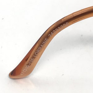 K&ouml;nnte beinhalten: Nahaufnahme der Innenseite eines braunen Metallrahmens einer Brille. Der Rahmen ist mit dem Text "47□19-135 LORRAINE 24233200" beschriftet.