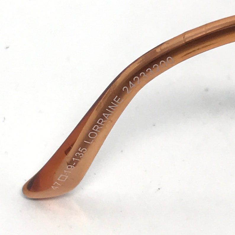 K&ouml;nnte beinhalten: Nahaufnahme der Innenseite eines braunen Metallrahmens einer Brille. Der Rahmen ist mit dem Text "47□19-135 LORRAINE 24233200" beschriftet.