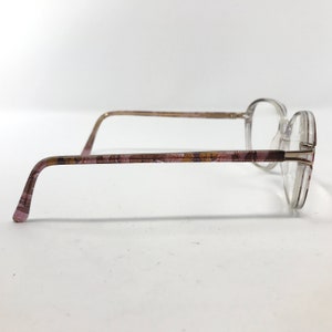 May include: Clear eyeglasses with a round frame and patterned temples. The temples feature a pink, brown, and gold floral design. The glasses are viewed from the side against a white background.