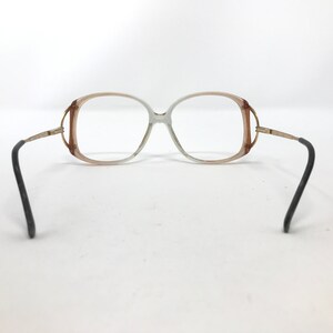 May include: Vintage eyeglasses with a light brown and clear frame, gold-tone accents, and black temples. The lenses are clear. The glasses have a retro, oversized design.