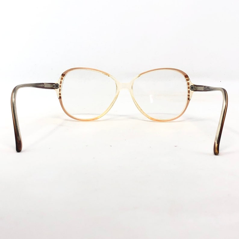 Puede incluir: Gafas vintage de gran tama&ntilde;o con montura marr&oacute;n claro y crema. Las gafas tienen forma redondeada y lentes transparentes. Las patillas son de color marr&oacute;n m&aacute;s oscuro. La montura tiene un detalle de rayas decorativas en los bordes exteriores.