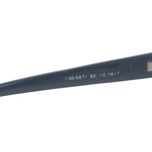 May include: Close-up of the inside of a dark gray frame of a pair of glasses. The frame has the text "138-5871 58□16 YW17" printed on it.