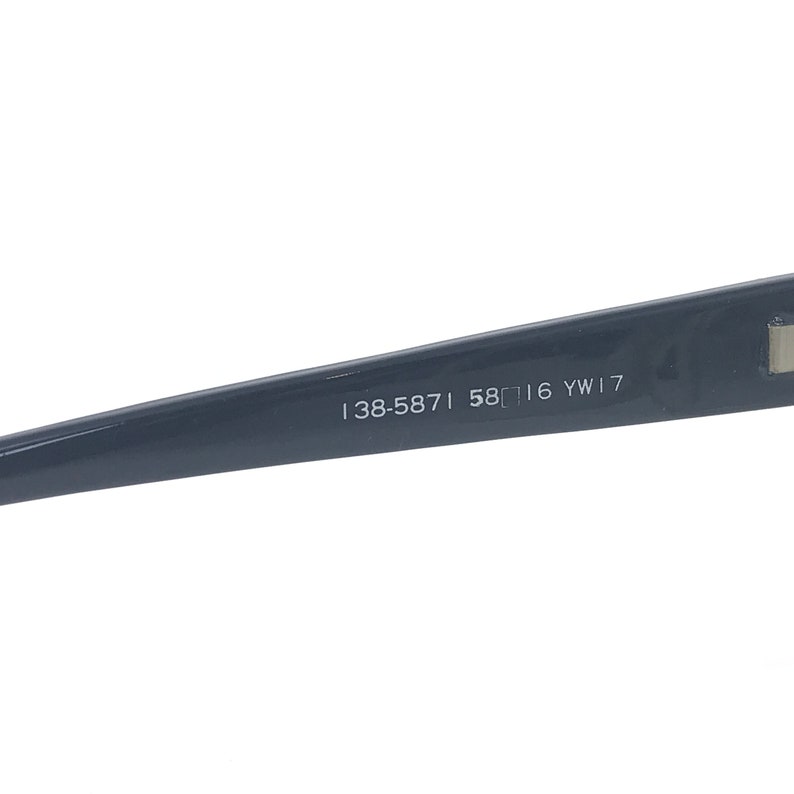 May include: Close-up of the inside of a dark gray frame of a pair of glasses. The frame has the text "138-5871 58□16 YW17" printed on it.