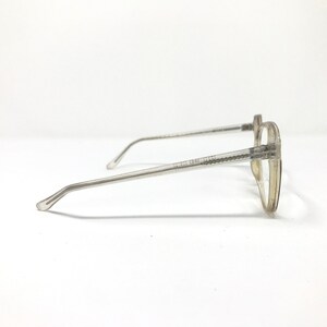 Puede incluir: Gafas transparentes con montura redonda y varillas finas de color gris claro. Las gafas tienen un dise&ntilde;o cl&aacute;sico, adecuado para el uso diario. El texto en la varilla dice "CALVIN KLEIN JEANS".