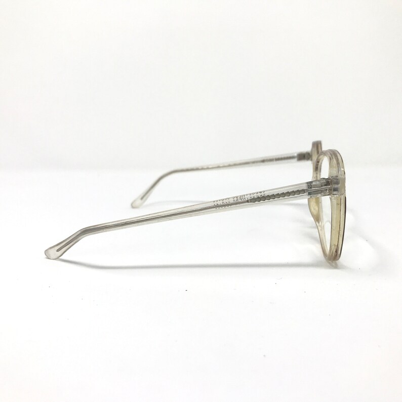 Puede incluir: Gafas transparentes con montura redonda y varillas finas de color gris claro. Las gafas tienen un dise&ntilde;o cl&aacute;sico, adecuado para el uso diario. El texto en la varilla dice "CALVIN KLEIN JEANS".