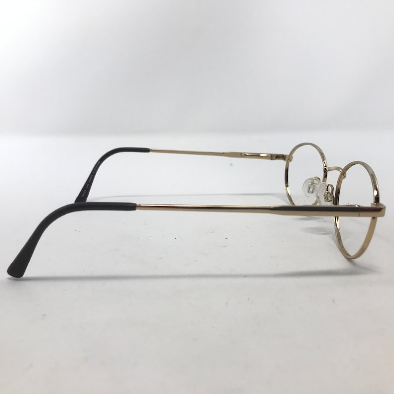 Pu&ograve; includere: Occhiali rotondi color oro con terminali neri. Gli occhiali hanno una sottile montatura in metallo e lenti trasparenti. La vista laterale mostra il design delicato e la forma delle lenti.