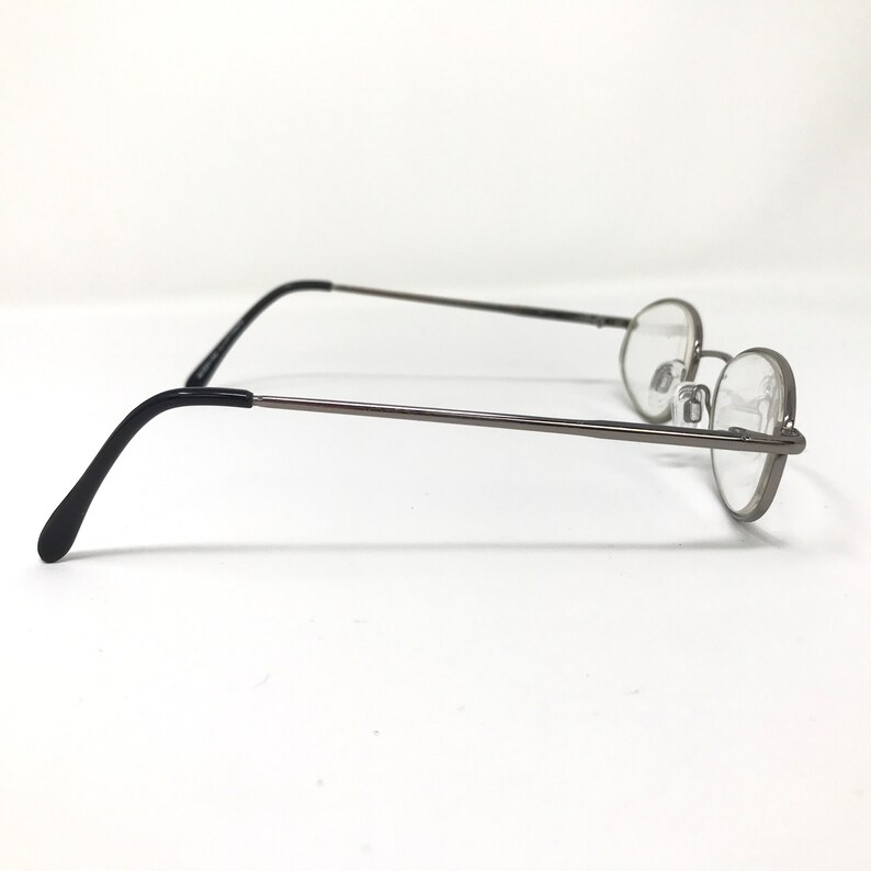 Op de afbeelding: Een bril met een dun, donkergrijs metalen montuur en ronde glazen. De pootjes zijn zwart en buigen naar beneden om achter de oren te rusten. De bril staat tegen een witte achtergrond.