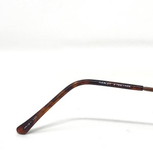 May include: Close-up of the temple arm of a pair of eyeglasses. The arm is a tortoiseshell pattern with the text "HARLEY 21661426" printed on the side. The end of the arm has the text "46021-14C" printed on it.