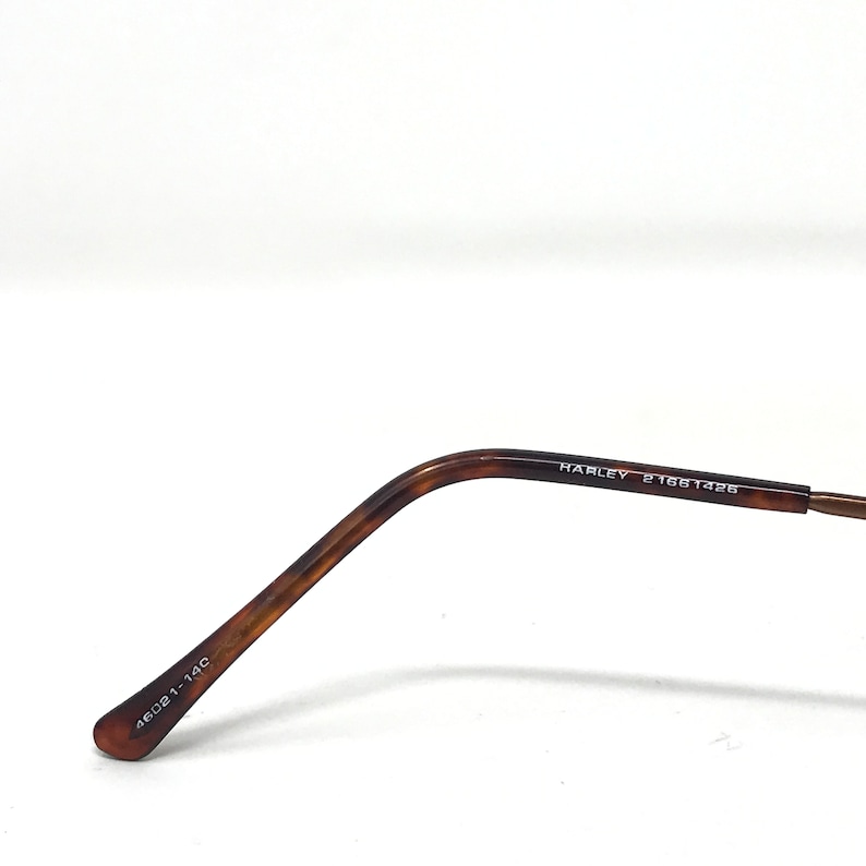 May include: Close-up of the temple arm of a pair of eyeglasses. The arm is a tortoiseshell pattern with the text "HARLEY 21661426" printed on the side. The end of the arm has the text "46021-14C" printed on it.