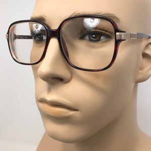 May include: Square-framed eyeglasses with a tortoiseshell pattern on the rims and temples. The glasses have clear lenses and gold-colored accents on the temples. The frames are set on a mannequin head.
