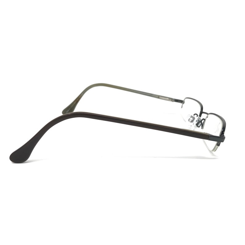 K&ouml;nnte beinhalten: Halbrandlose Brille mit dunkelbraunem Rahmen und B&uuml;geln. Die Gl&auml;ser sind klar, und die Nasenpads sind sichtbar. Die Brille ist vor einem wei&szlig;en Hintergrund platziert.
