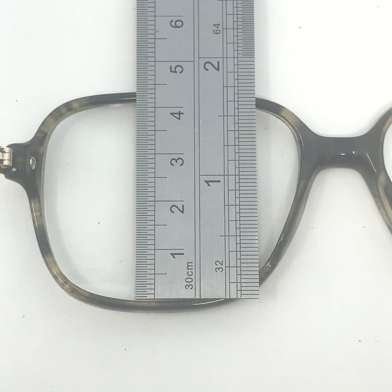 Puede incluir: Primer plano de gafas con estampado de carey. Se coloca una regla met&aacute;lica junto a la montura, midiendo aproximadamente 5 cm de altura. Las gafas tienen forma cuadrada y est&aacute;n sobre un fondo blanco.