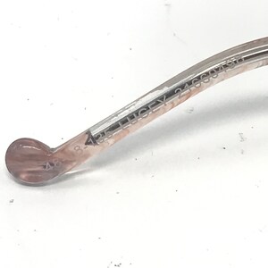 May include: Close-up of a section of eyeglasses. The frame is a light brown colour with the text "LUCKEY 24660496" and "48-4" printed on the arm. The end of the arm has a rounded, light brown tip.