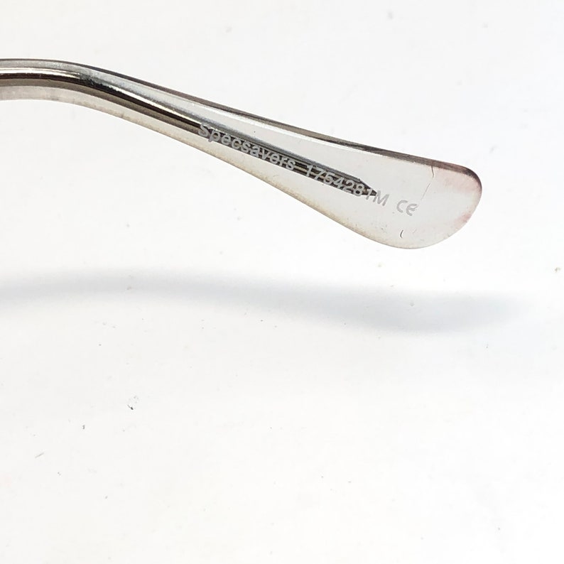 K&ouml;nnte beinhalten: Nahaufnahme des B&uuml;gels einer Brille. Der Rahmen ist aus silberfarbenem Metall. Der Text "Specsavers 175428M ce" ist auf der Innenseite des B&uuml;gels aufgedruckt.