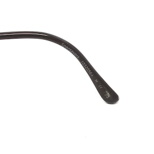 May include: Close-up of a black eyeglass arm with the text "Specsavers 1032056+ M ce P22" printed in white. The arm is curved and has a glossy finish. The background is white.
