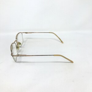 May include: A pair of eyeglasses with a gold-colored metal frame. The lenses are clear, and the temples have a light brown plastic coating. The glasses are set against a white background.